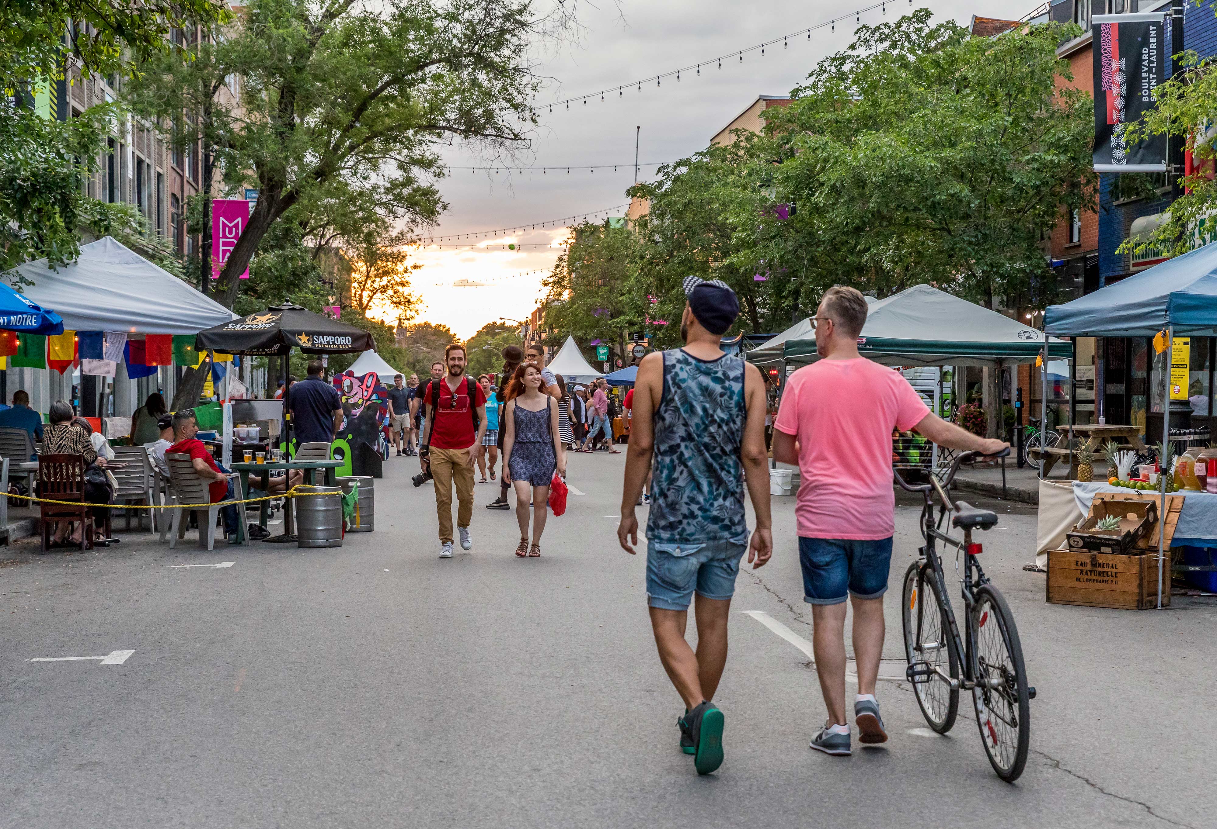 a group of people walking down a street with tents and trees